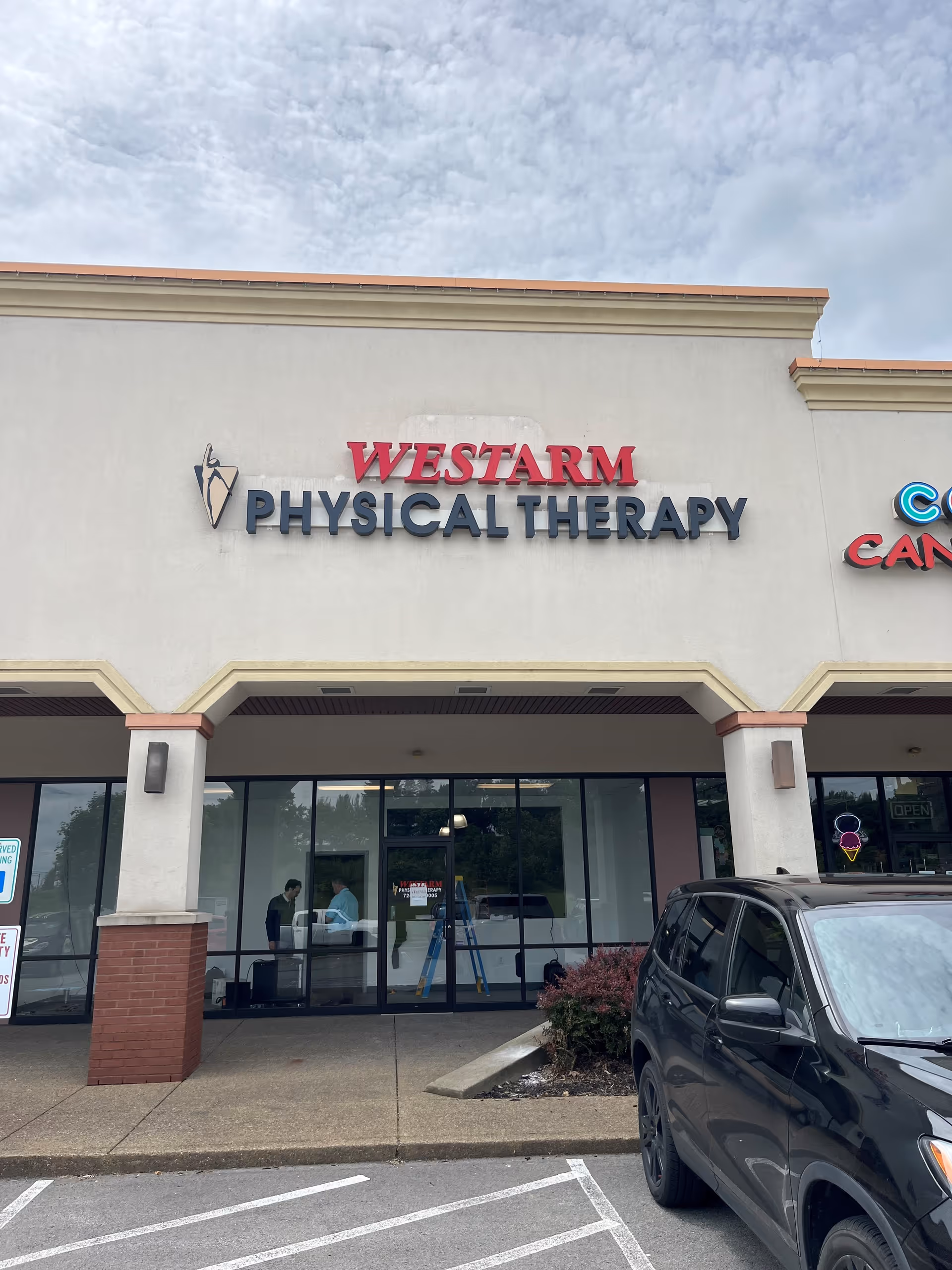 Front of WESTARM Physical Therapy building with large sign, glass doors, and a parked car.