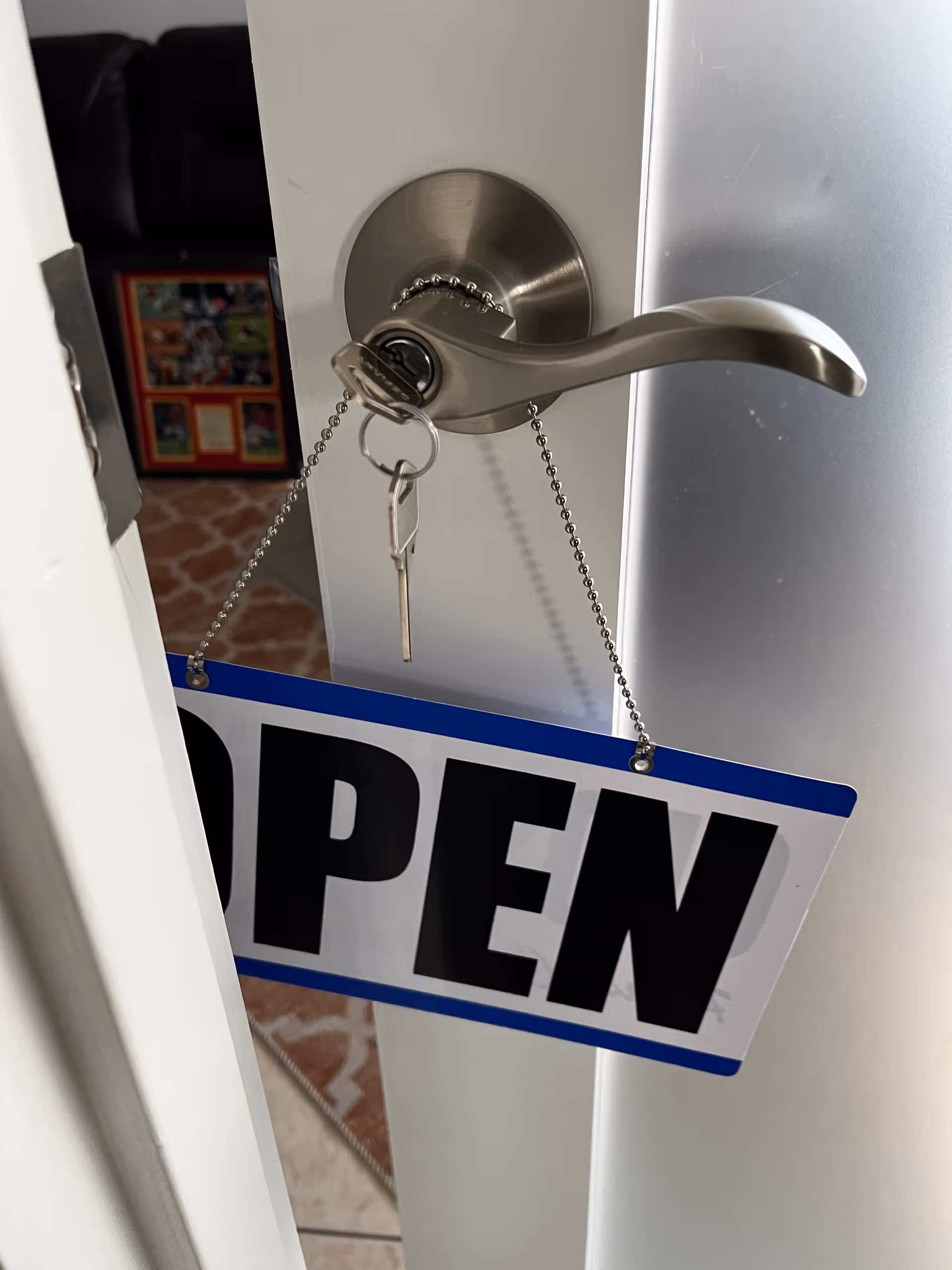 Open door with handle and hanging OPEN sign, keys on the lock.
