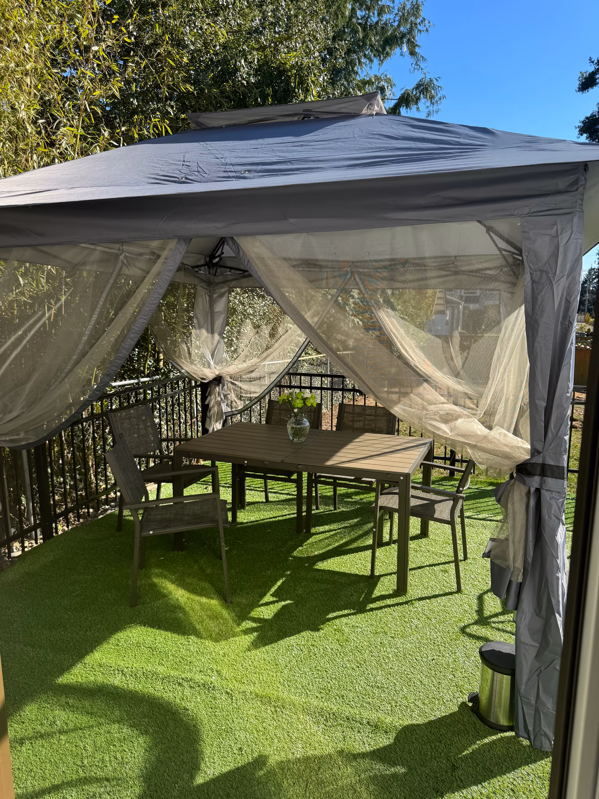 Outdoor balcony gazebo with a dining table, chairs, and billowing sheer curtains.