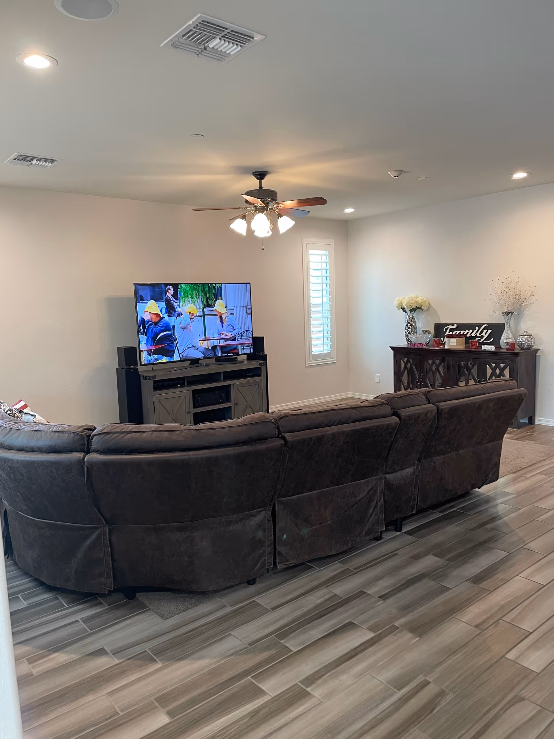 Cozy living room with a large curved sofa, TV, ceiling fan, and console.
