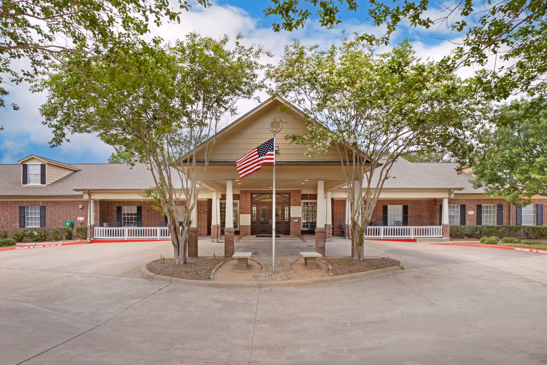 Windermere Estates Senior Living exterior featuring brick facade, flag, trees, and a circular driveway.