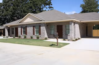 Single-story brick building with green shutters, front walkway, mailbox, and landscaped yard.