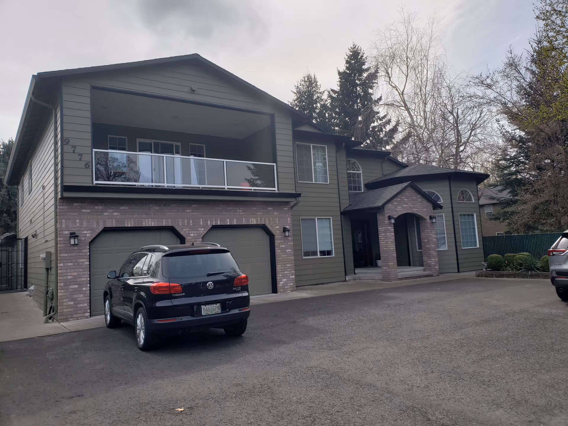 Two-story building with brick base, balcony, and a parked SUV in the driveway.