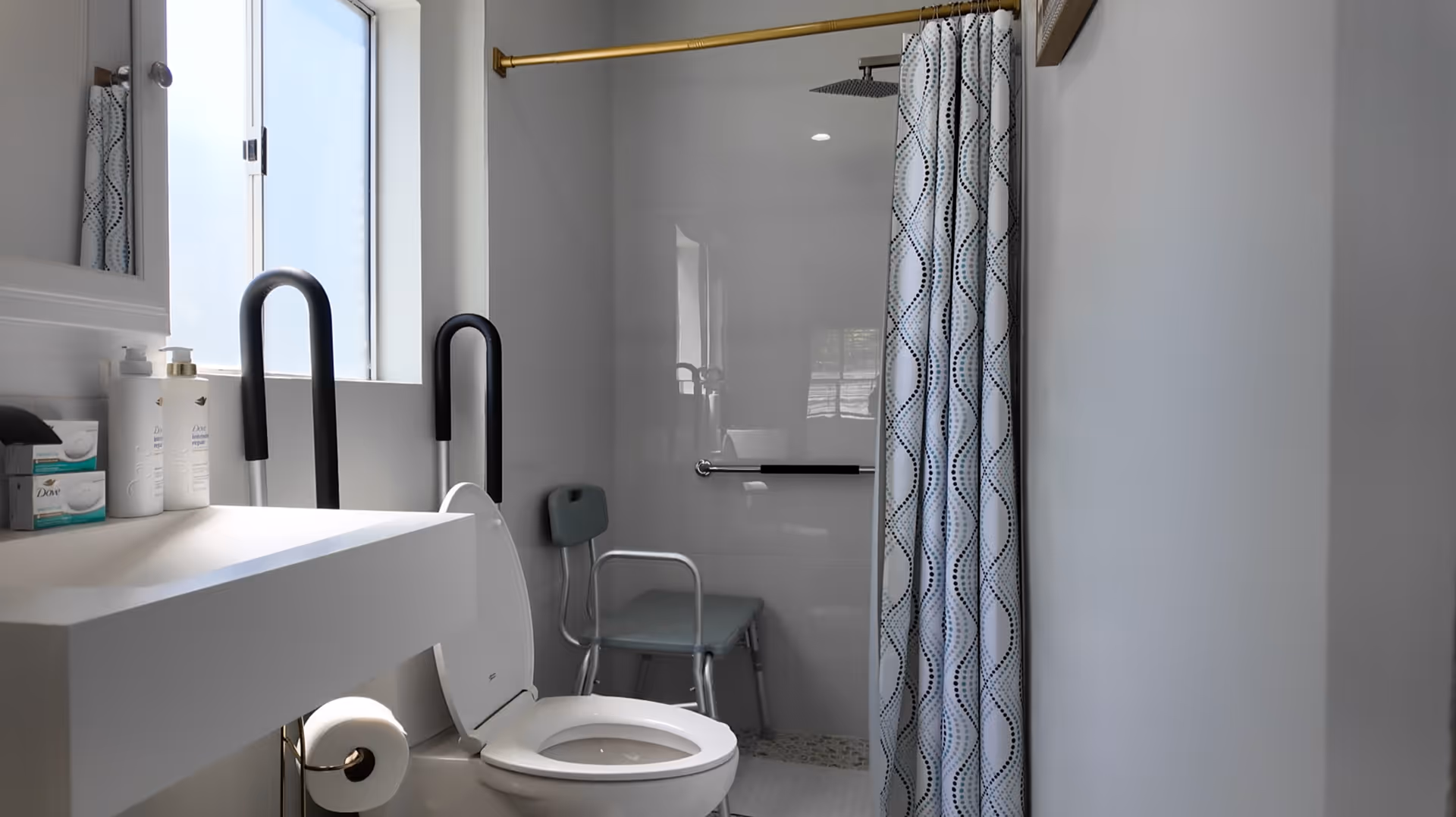 Accessible bathroom with toilet, sink, grab bars, shower, and shower chair in a clean space.
