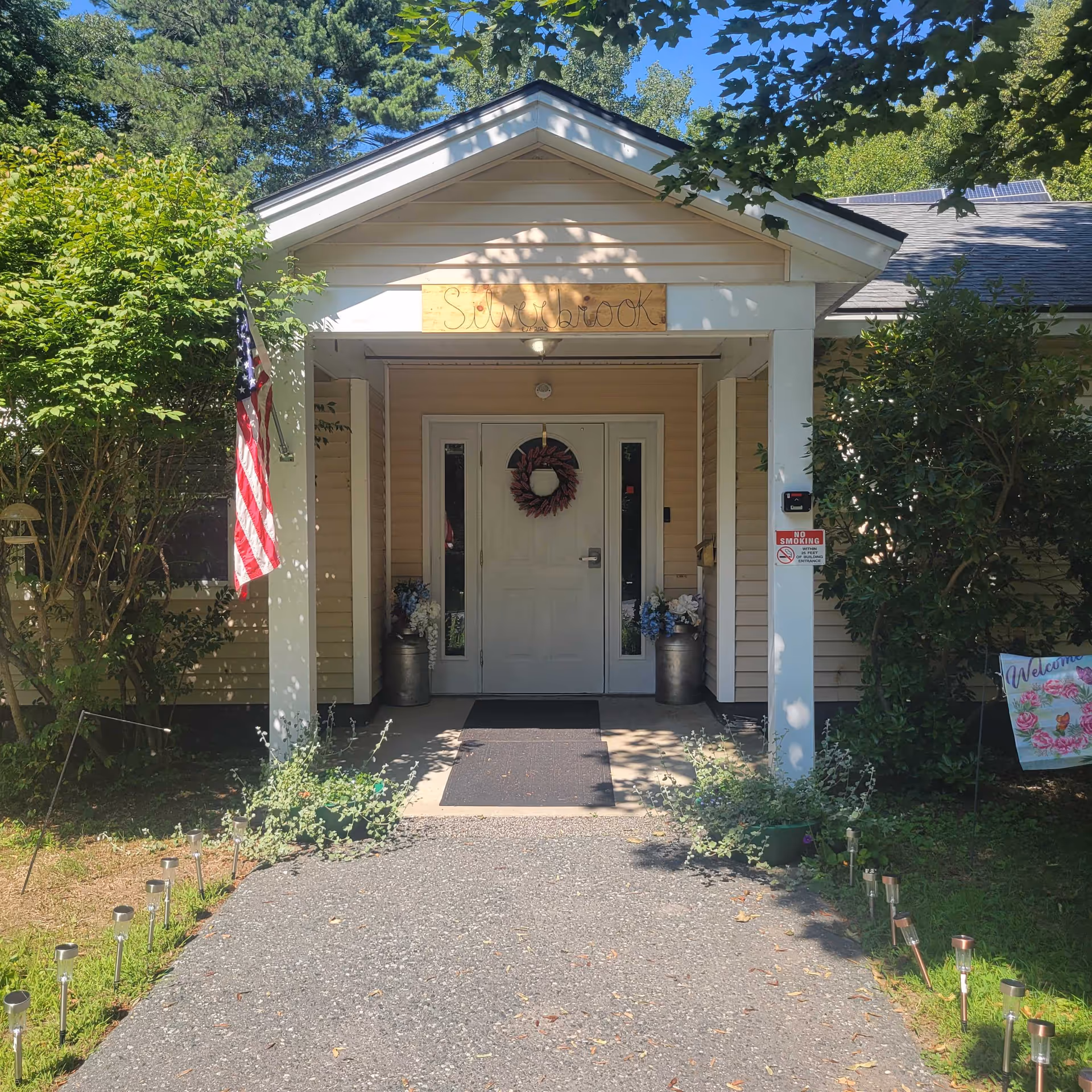 Front entrance of Silverbrook senior living facility with wreath, flag, and potted plants.
