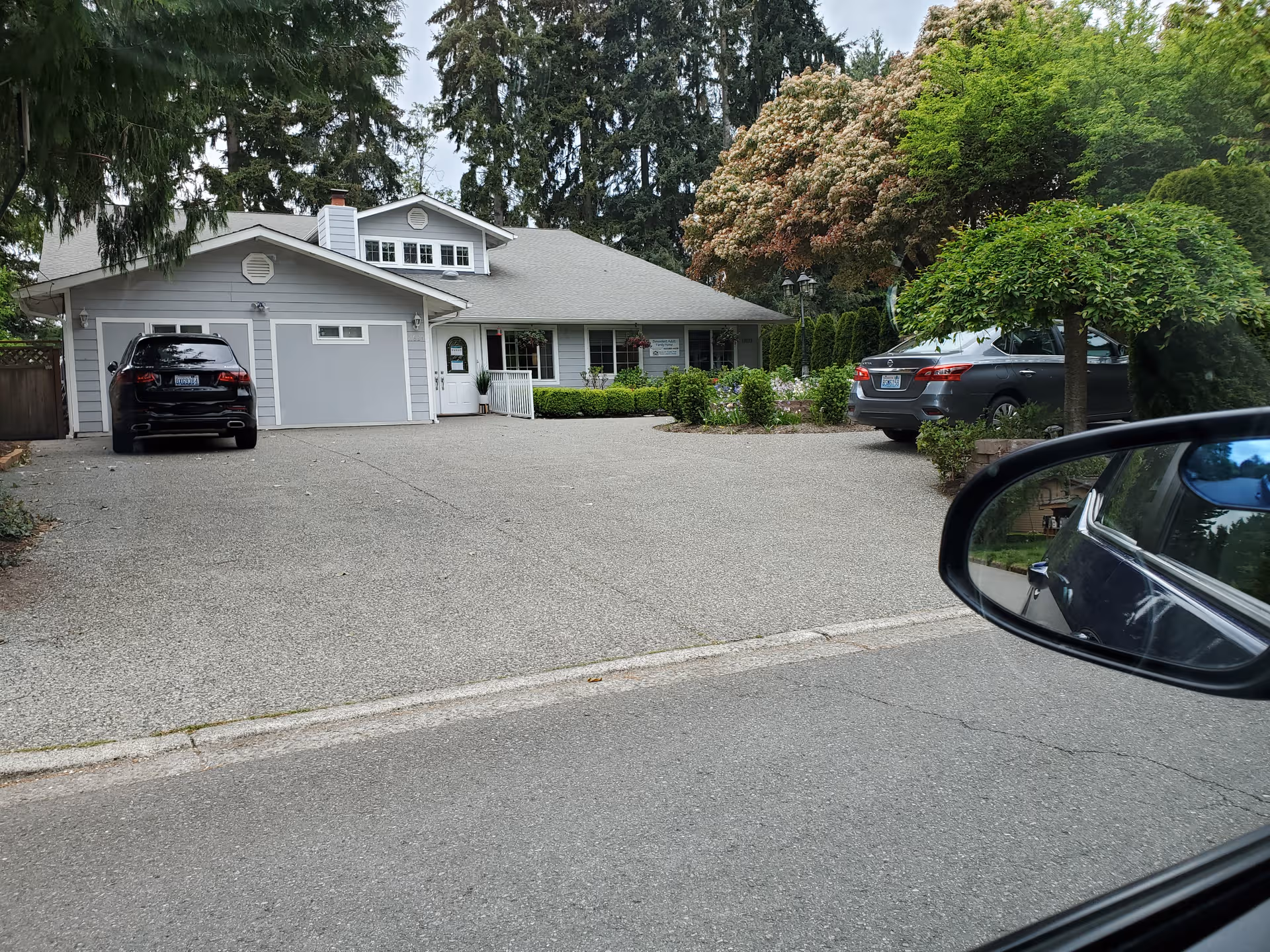 Gray, single-story senior living facility with a driveway and parked cars in front.