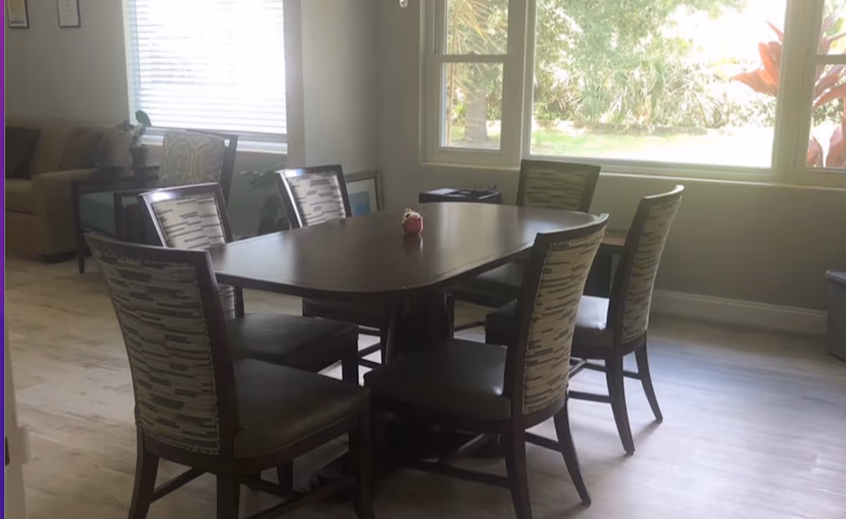 A dining table with six patterned chairs in a bright sunlit room.