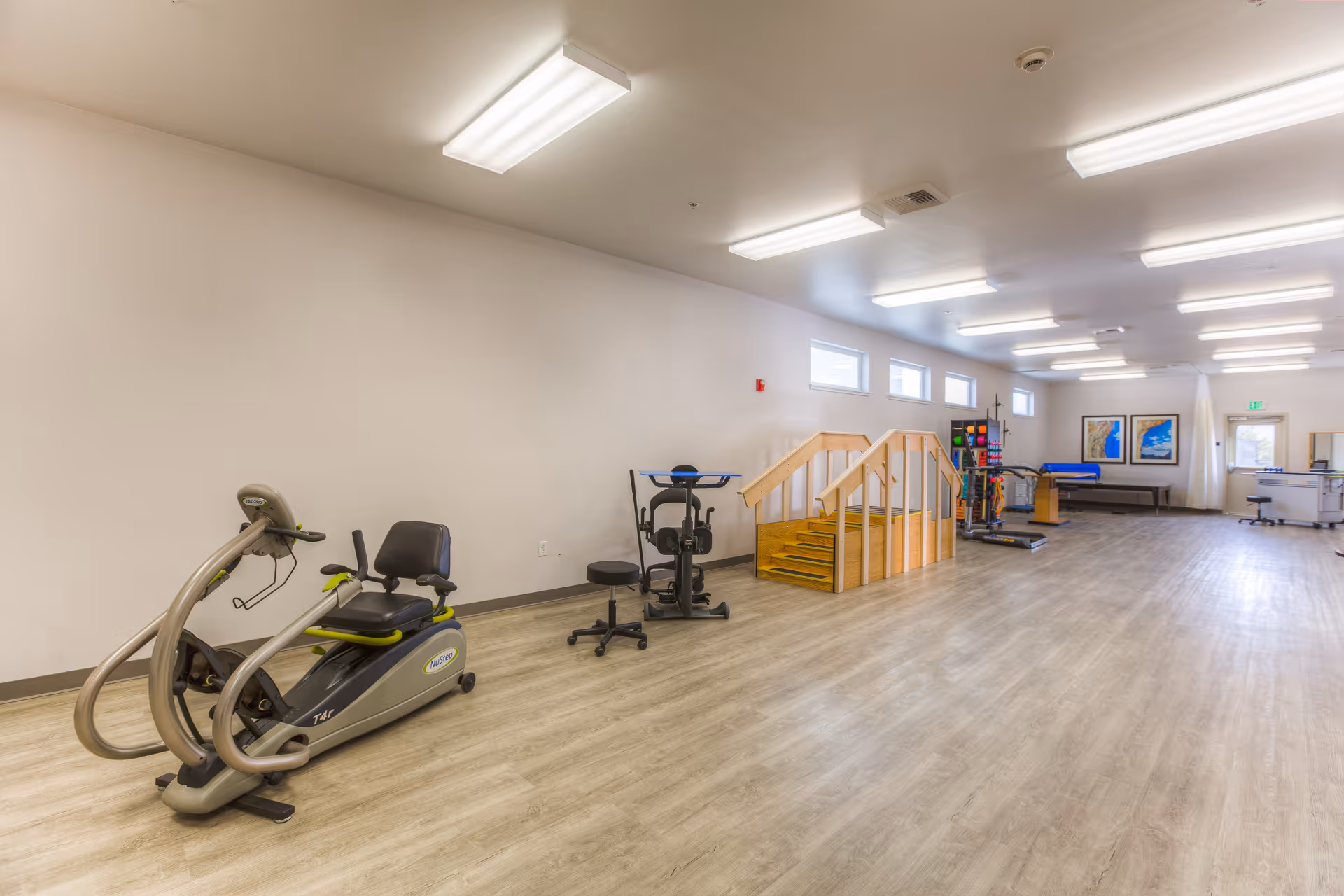 A spacious rehabilitation gym with exercise equipment, a wooden stair setup, and open floor area.