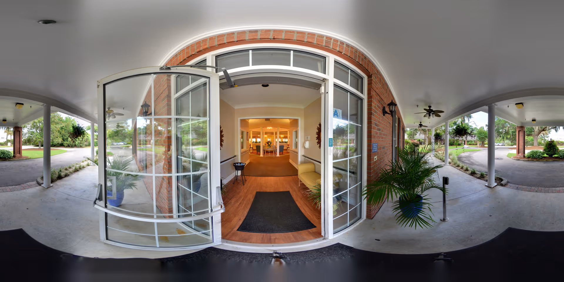 Covered porte-cochere with an open glass double door leading into a lobby with seating and potted plants.