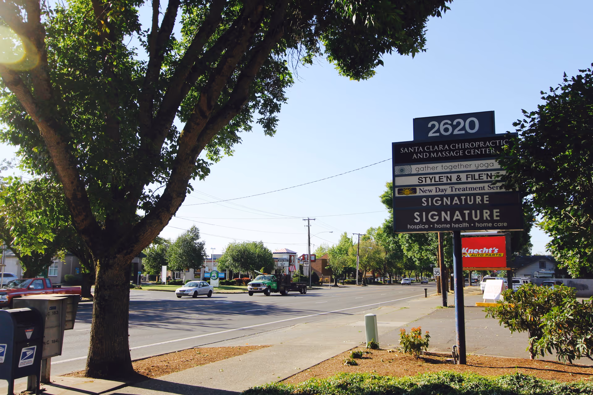 Outdoor street view featuring a tall signboard and leafy trees along a sunny roadway.