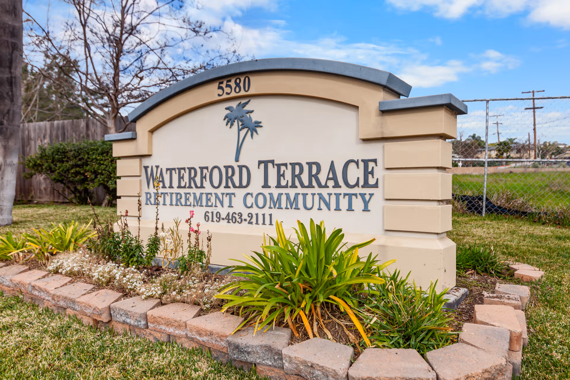 Exterior sign for Waterford Terrace Retirement Community with landscaped border and blue sky.