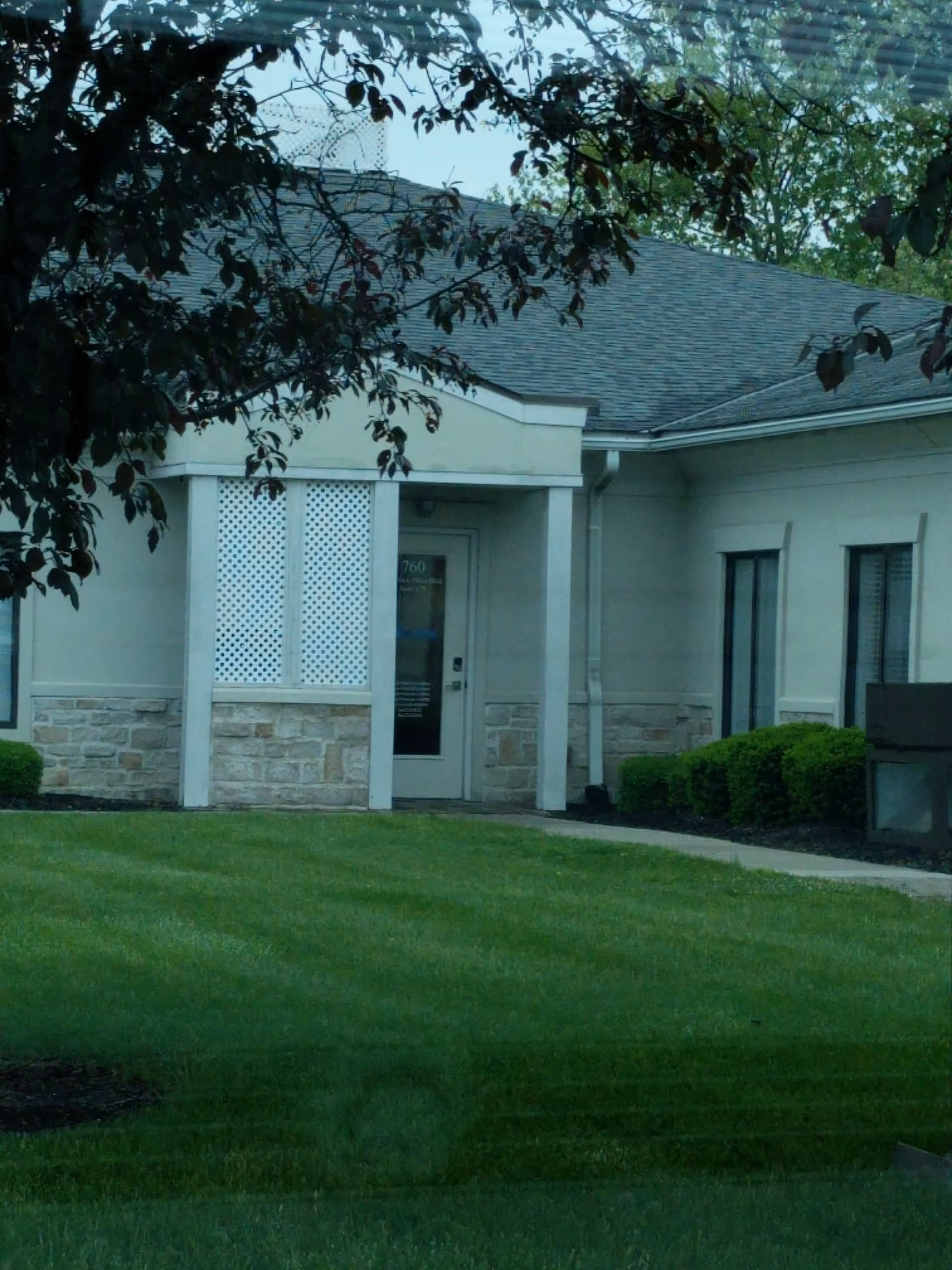 Exterior view of a single-story senior living facility entrance with lawn and trees