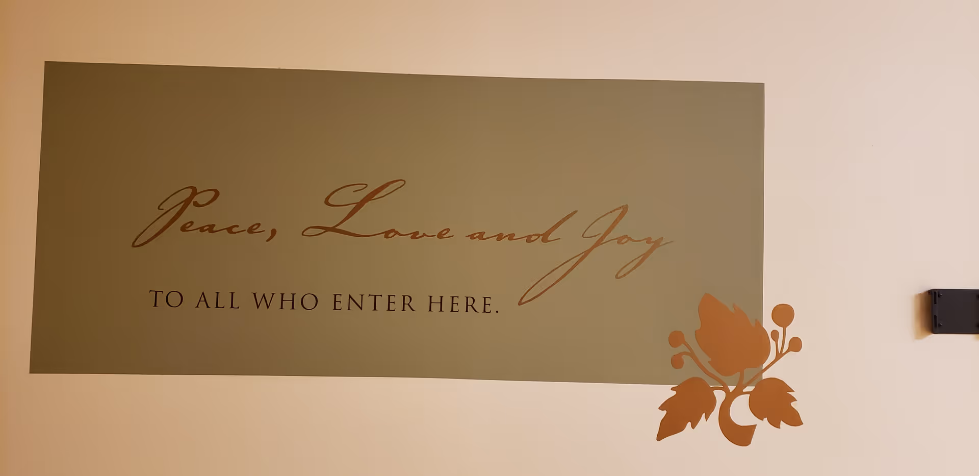Light-colored wall with a decorative sign reading Peace, Love and Joy, plus a floral corner.