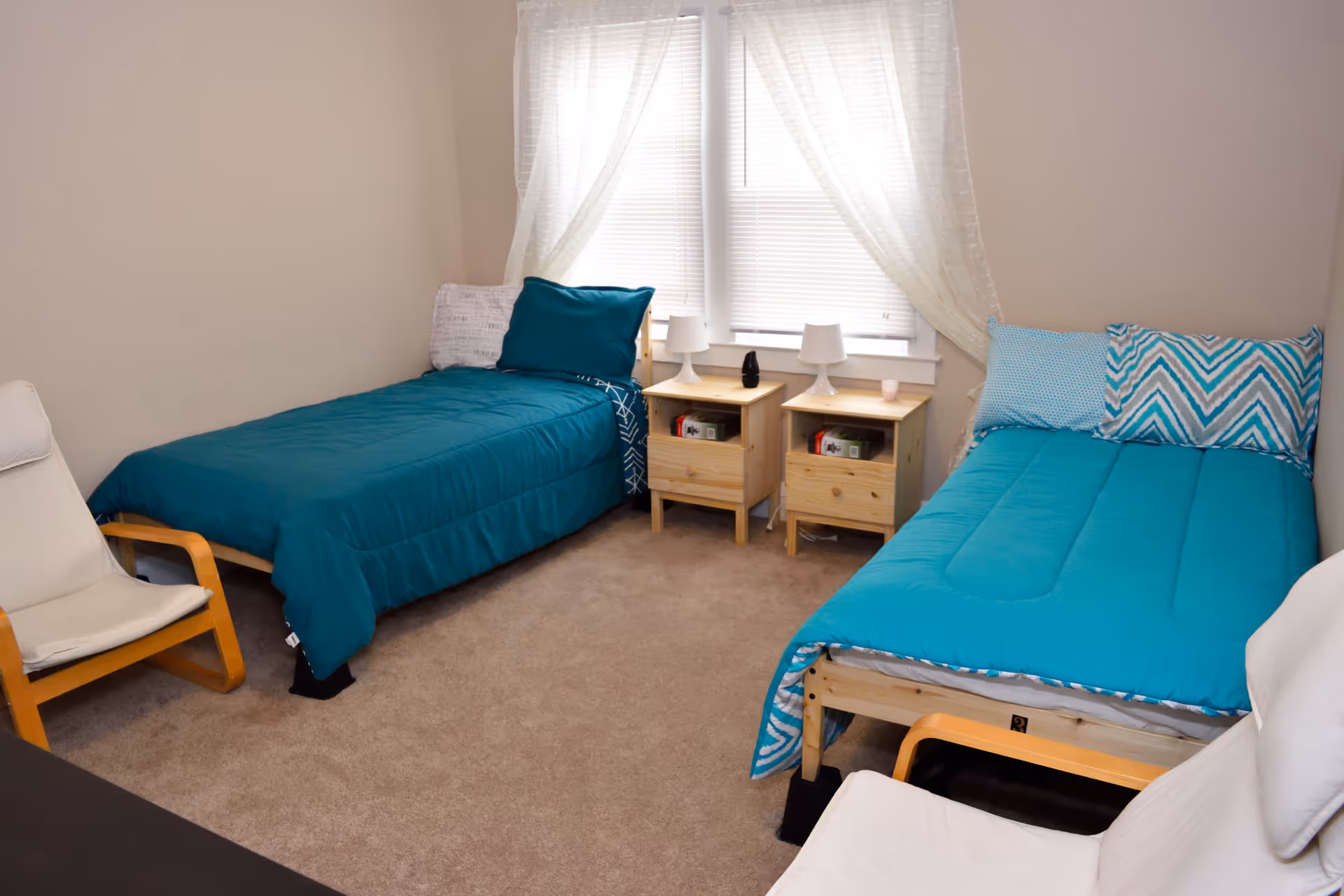 Two twin beds with teal bedding and matching nightstands in a bright shared bedroom.