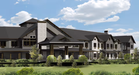Exterior view of a large senior living facility building with multiple windows, a covered entrance, and surrounded by greenery under a partly cloudy sky.