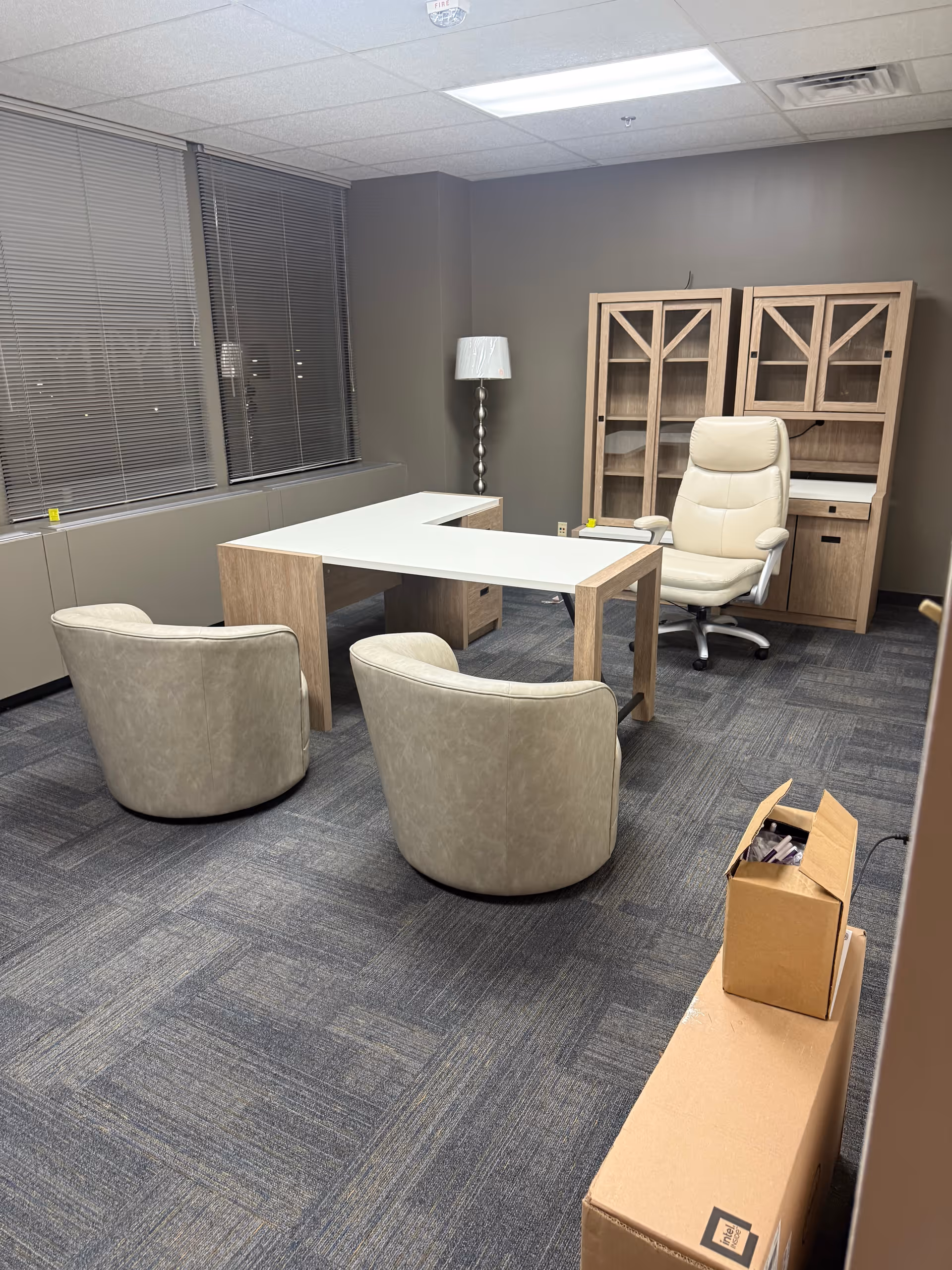 A modern interior office space with desk, chairs, cabinet, lamp, and large windows.