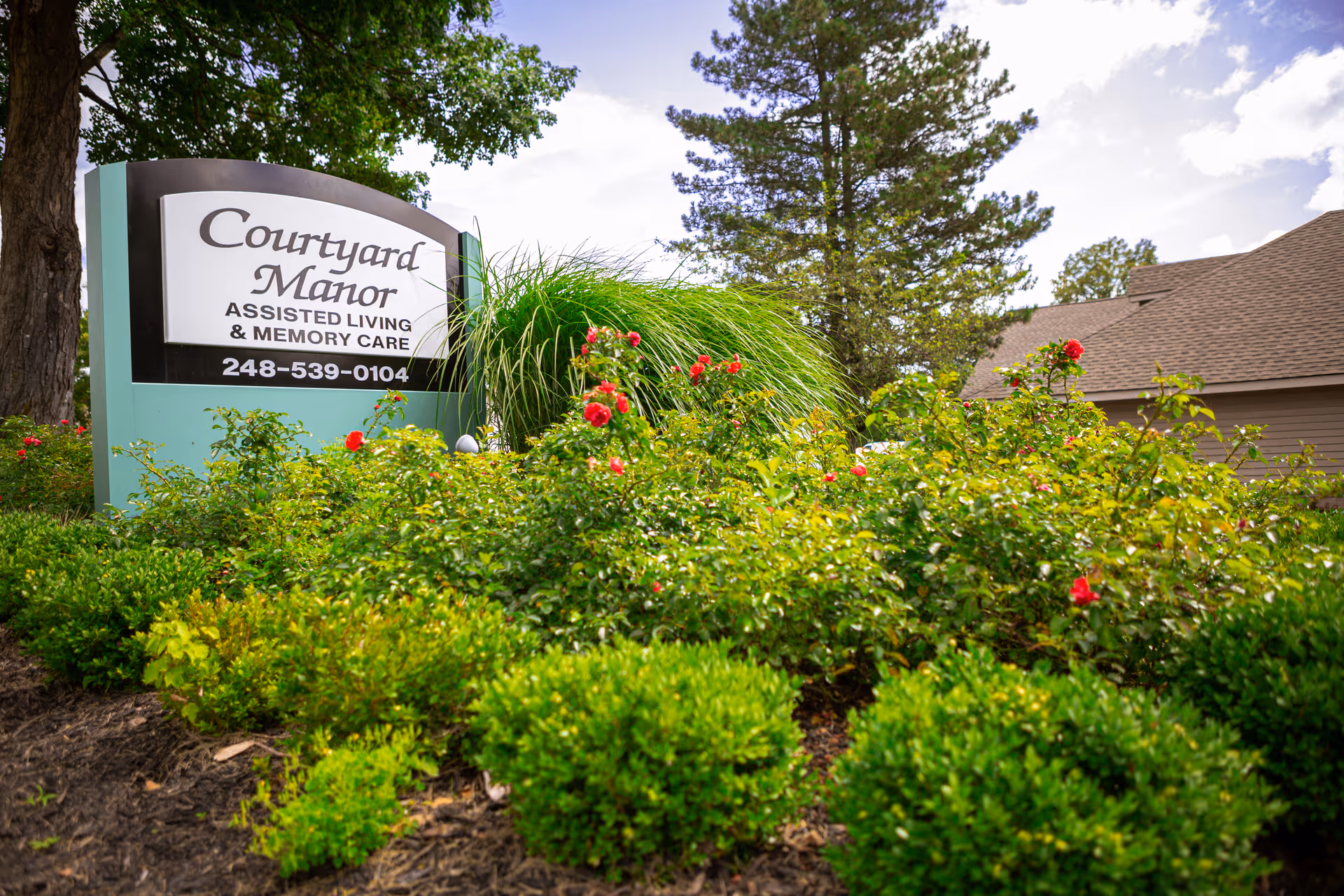 Courtyard Manor sign amid lush shrubs at the facility's exterior entrance.