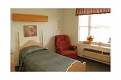 A cozy bedroom with a bed, red chair, window, and dresser in soft decor