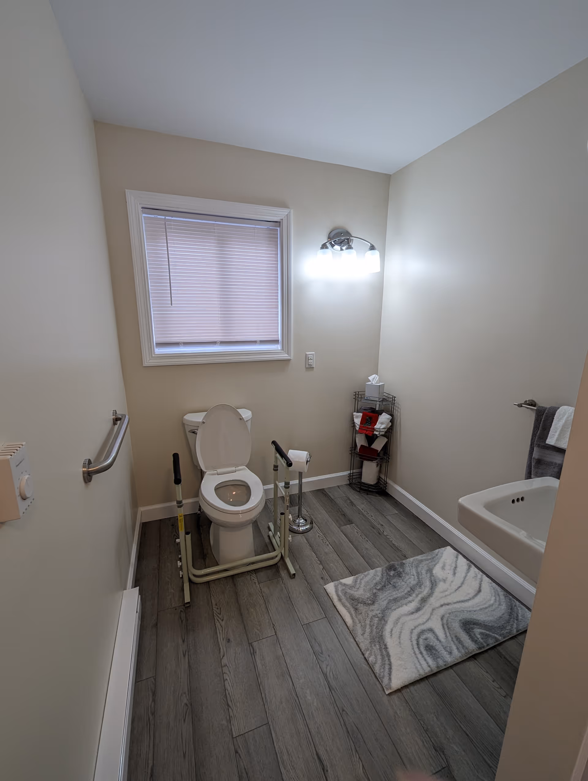 Accessible senior bathroom with grab bars, toilet frame, window, and towel rack.