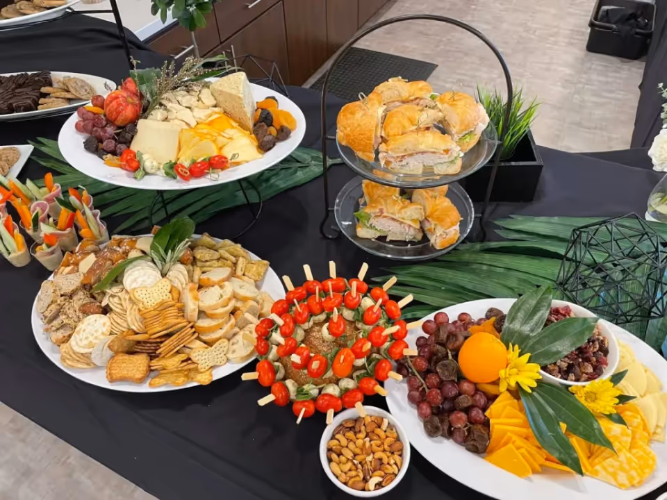 Assorted cheeses, crackers, fruit, and sandwiches arranged on a black-draped buffet table.