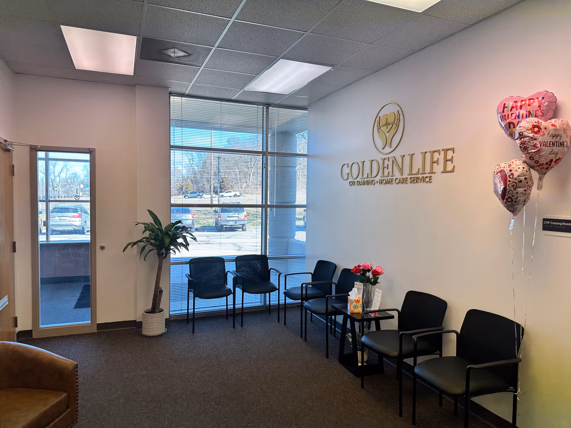 Lobby waiting area with black chairs, potted plant, and Golden Life sign on wall.
