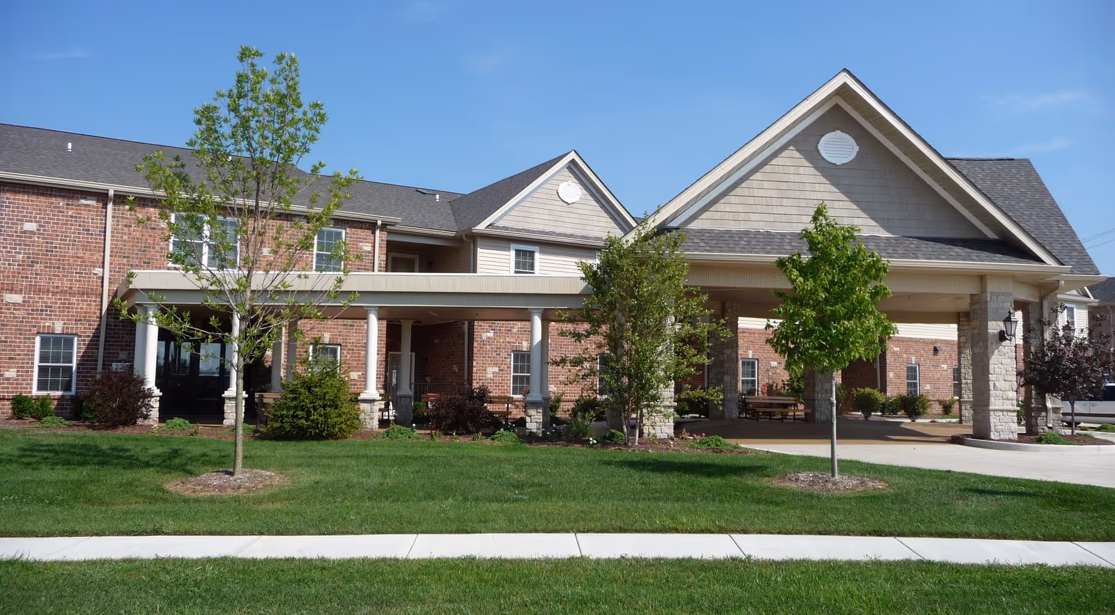 Front exterior of a brick senior living building with a covered entrance, columns, and landscaped lawn.