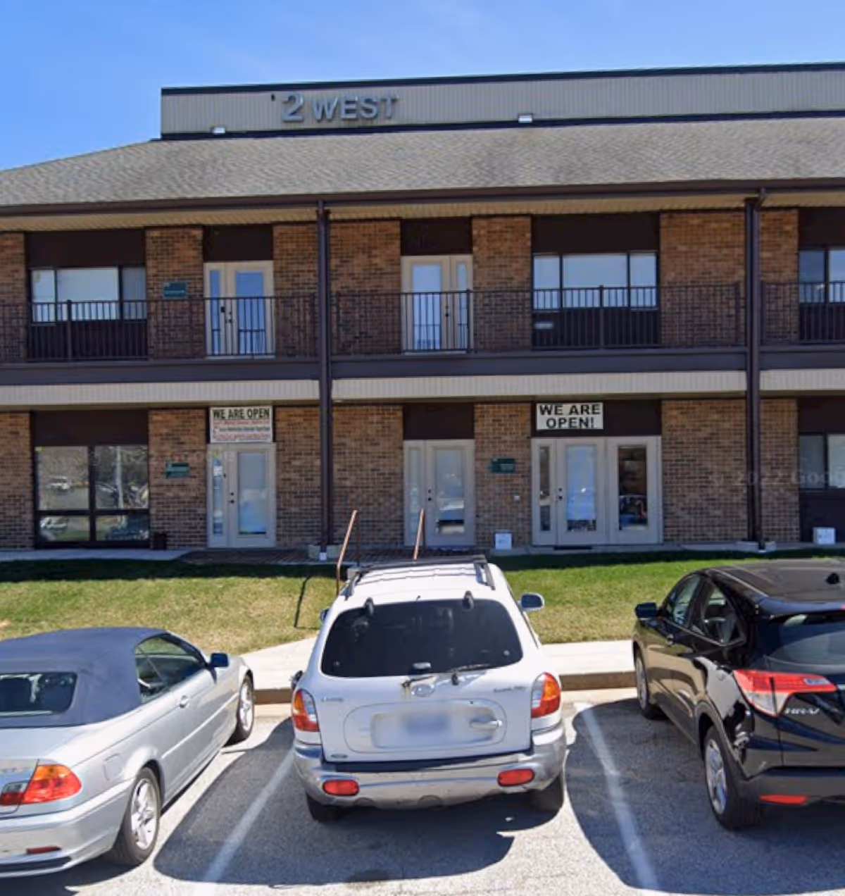 Brick senior living facility exterior with parked cars and two entrance doors.