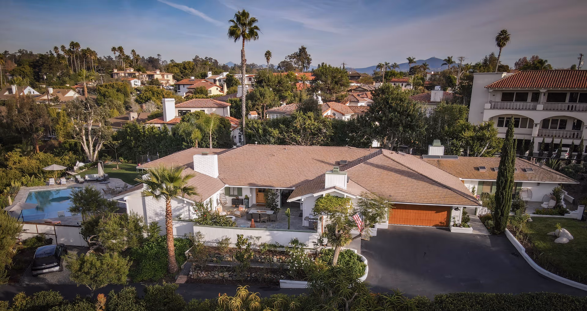 A single-story senior living facility with a tile roof, palm trees, driveway, and pool.