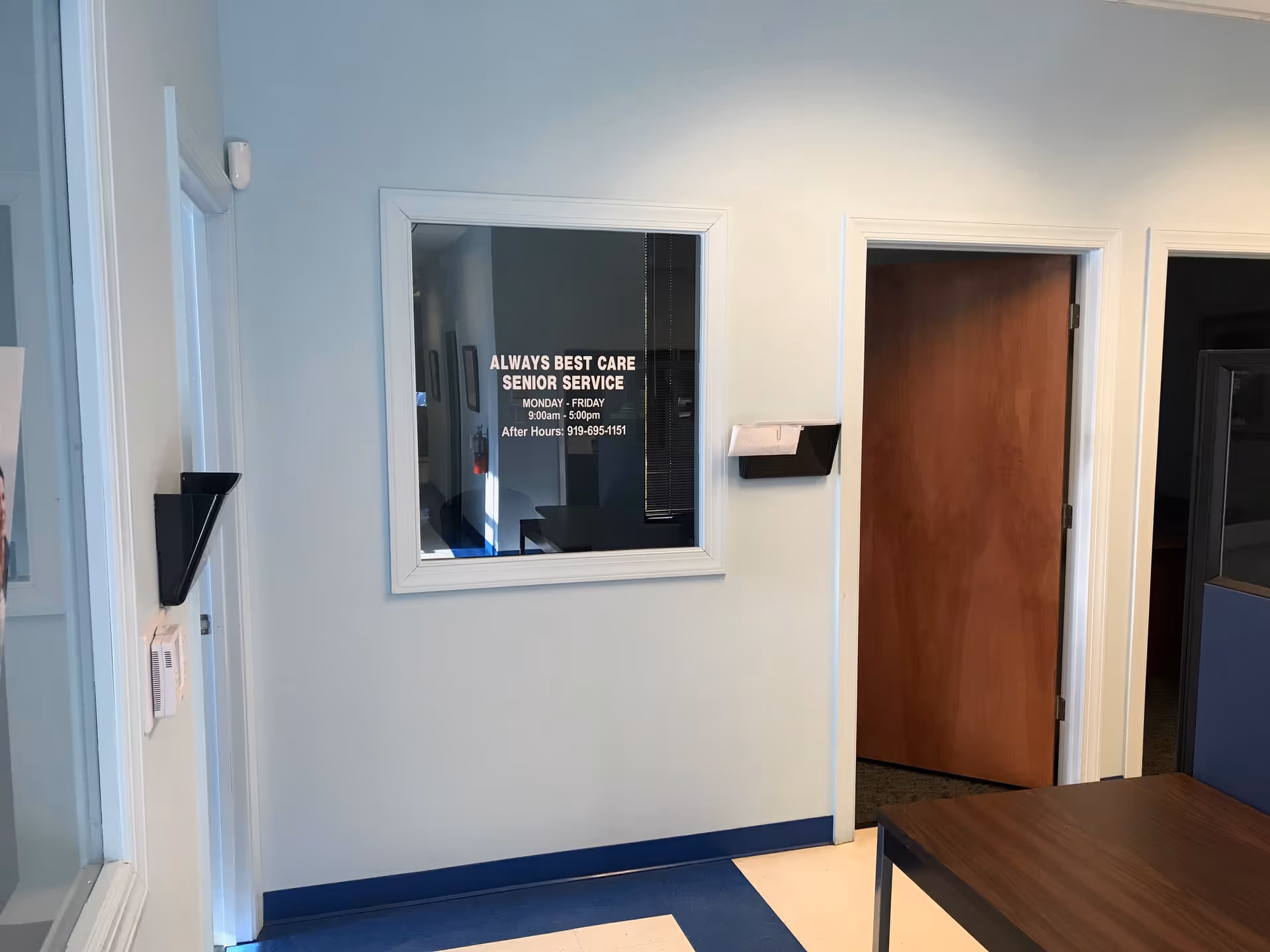 Interior office area featuring a windowed reception and doorway beside Always Best Care Senior Service sign.