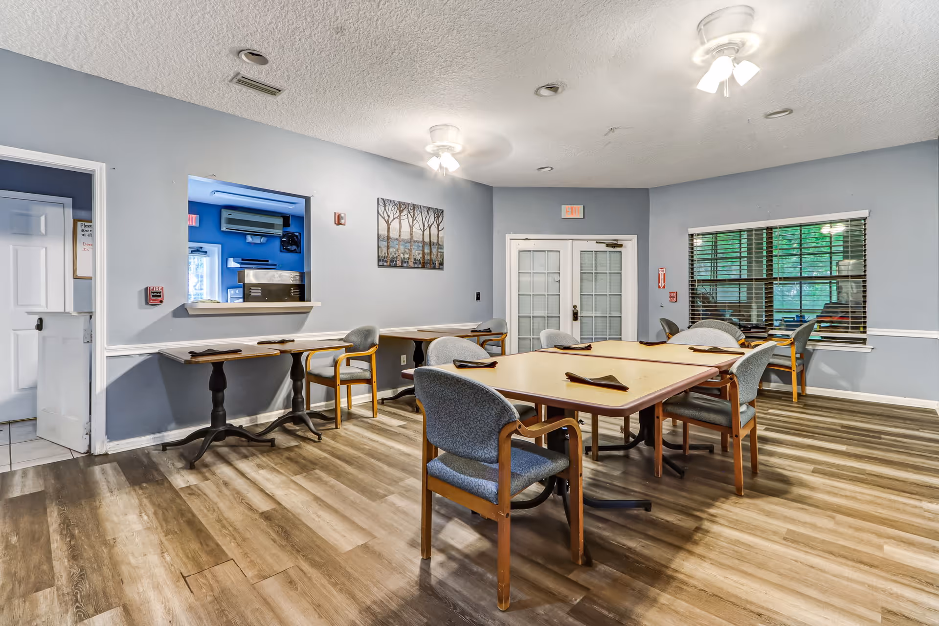 Bright dining area with several tables and chairs, a service counter, and blue walls.