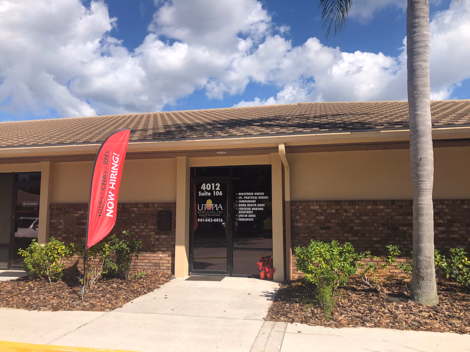 Front entrance of Utopia Home Care facility with glass doors, brick facade, and a red banner.