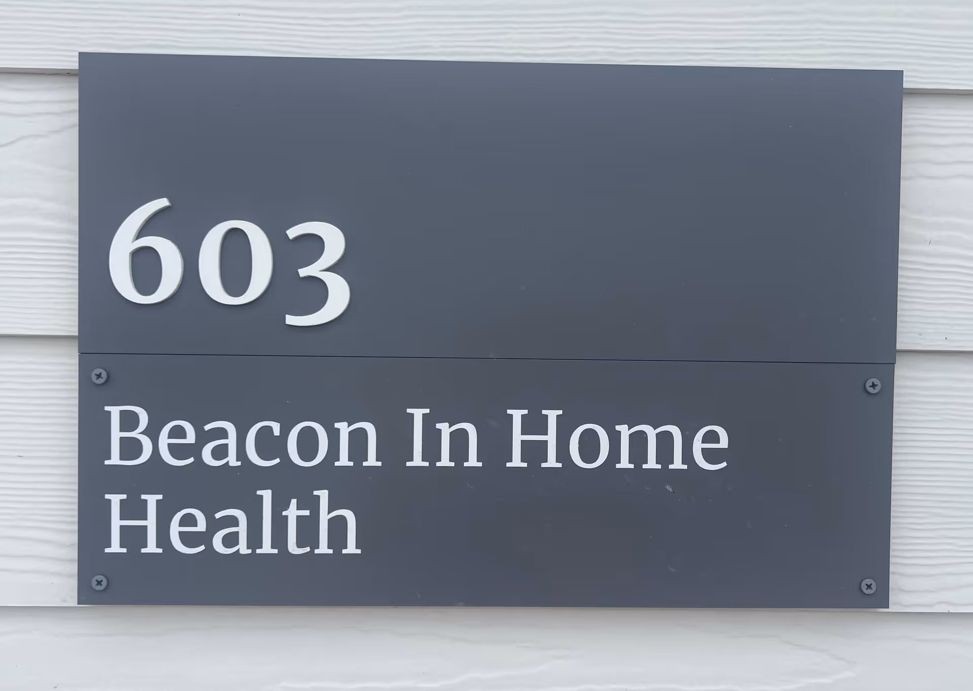 Gray two-panel sign reading 603 and Beacon In Home Health mounted on siding