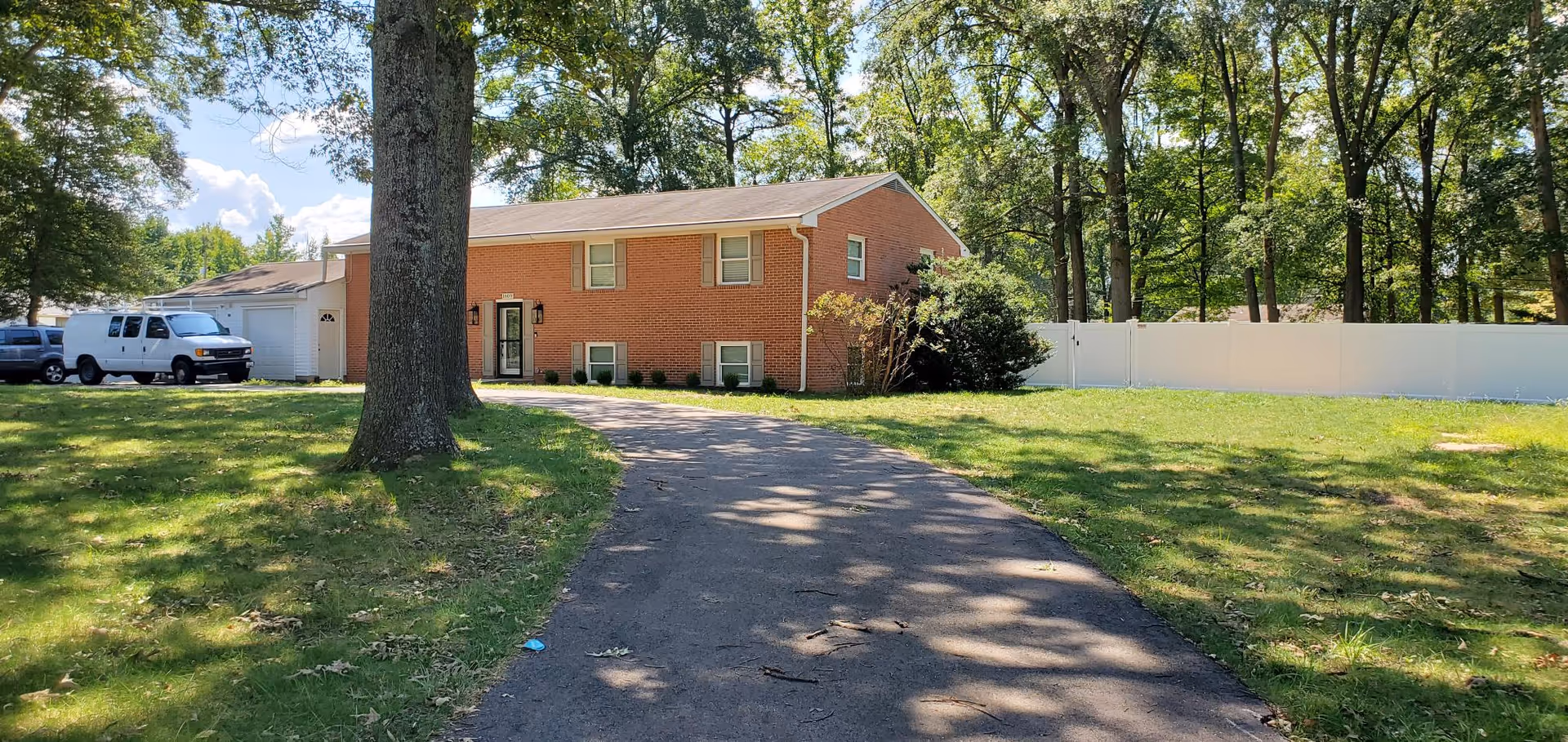 Brick, single-story building with driveway, white fence, and a parked van in front yard.