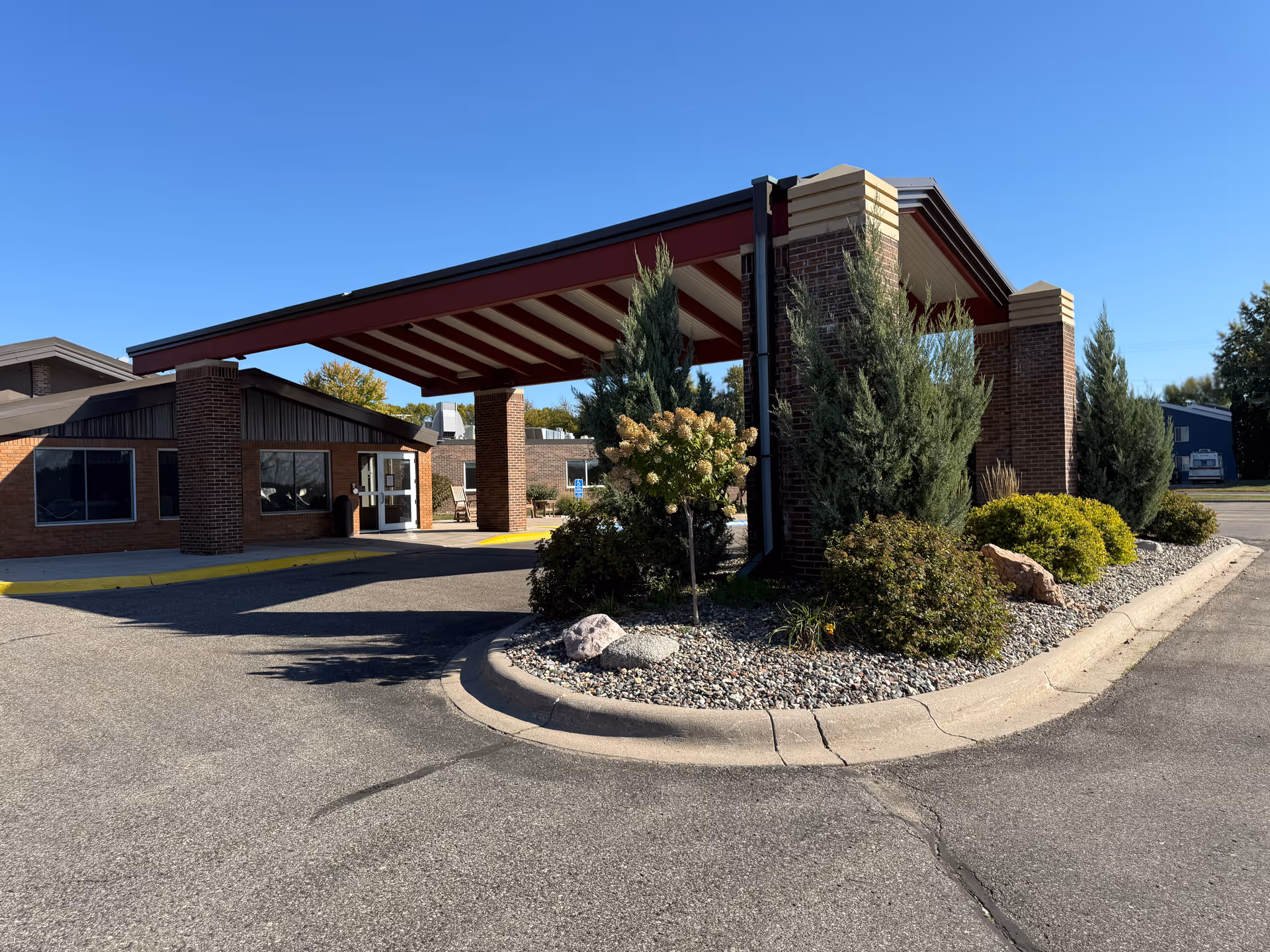 Exterior view of Cokato Manor entrance with a red brick porte-cochere and landscaped area.