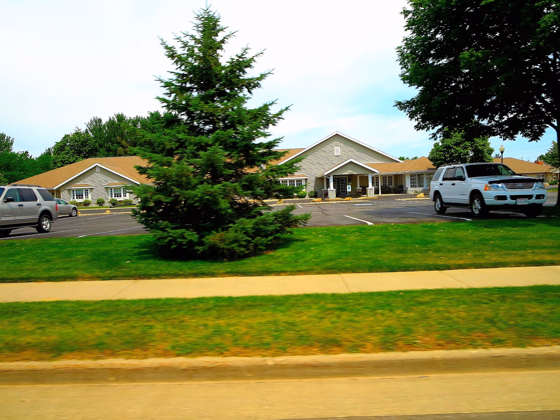 Exterior view of Pines Assisted Living building with parking lot and trees.