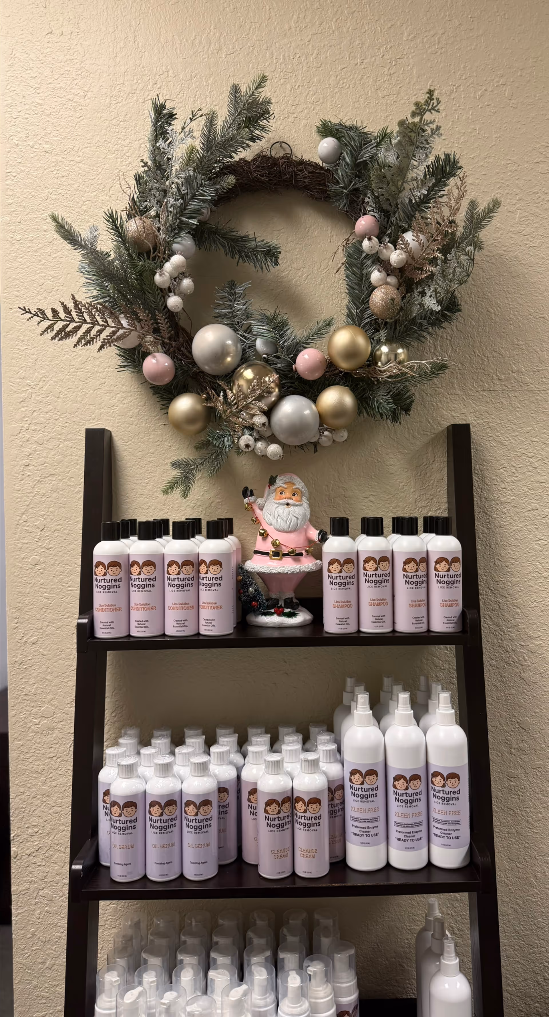 Shelf of Nurtured Noggins lice treatment bottles under a holiday wreath