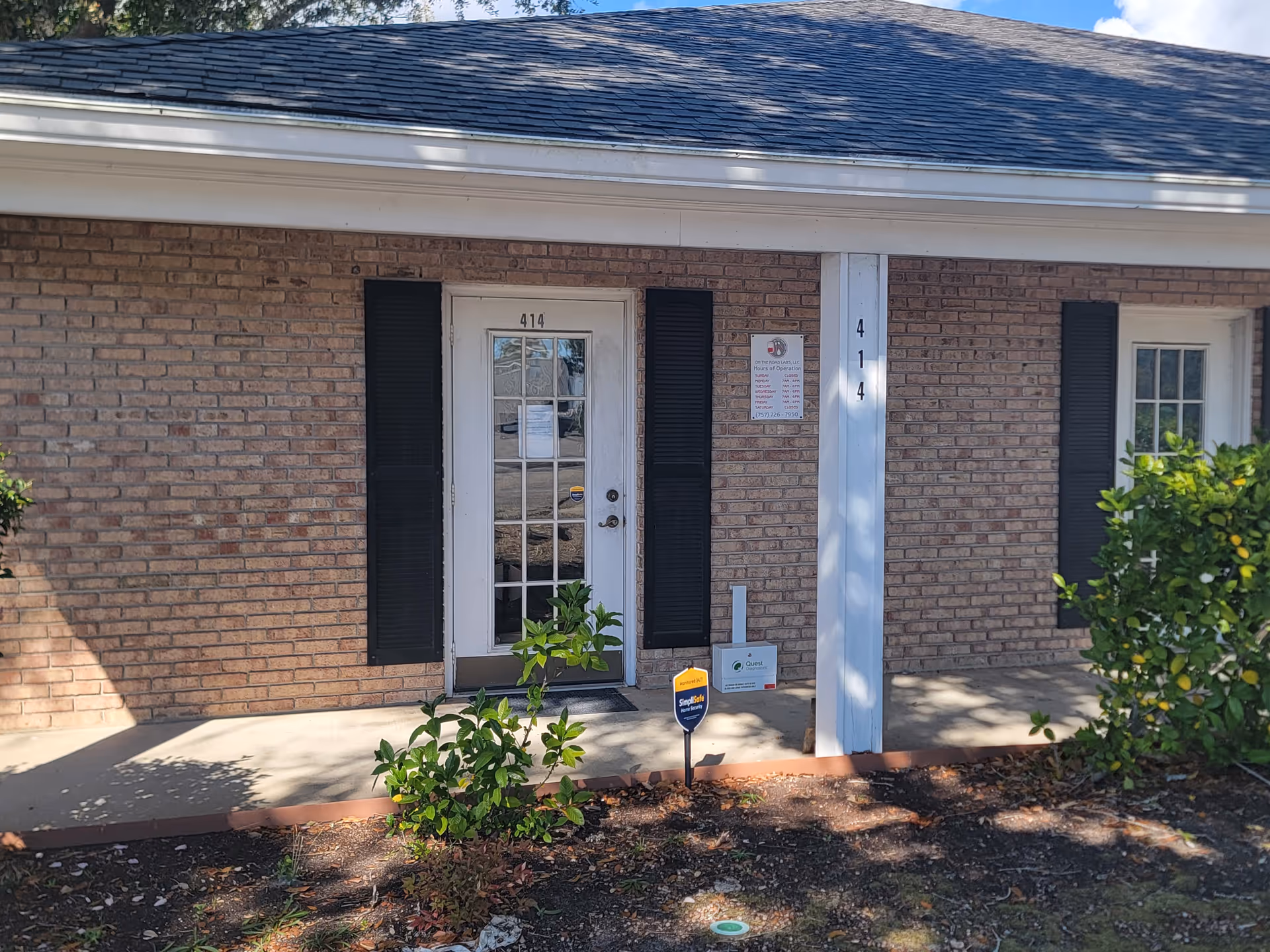 Front exterior of a brick building with a glass-paneled door and black shutters.