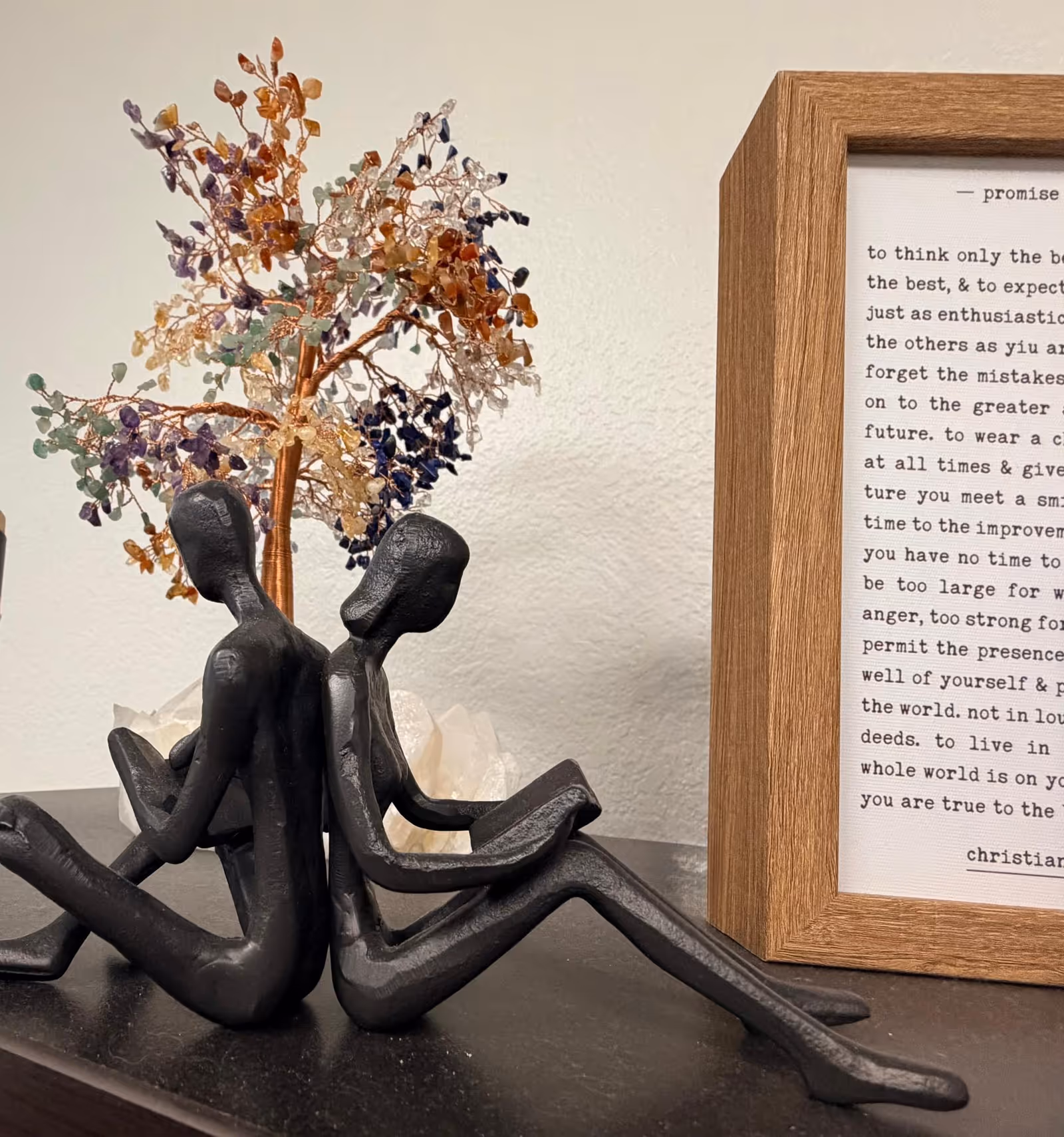 Abstract metal duo sculpture sits beside a wooden-framed text print on a shelf.