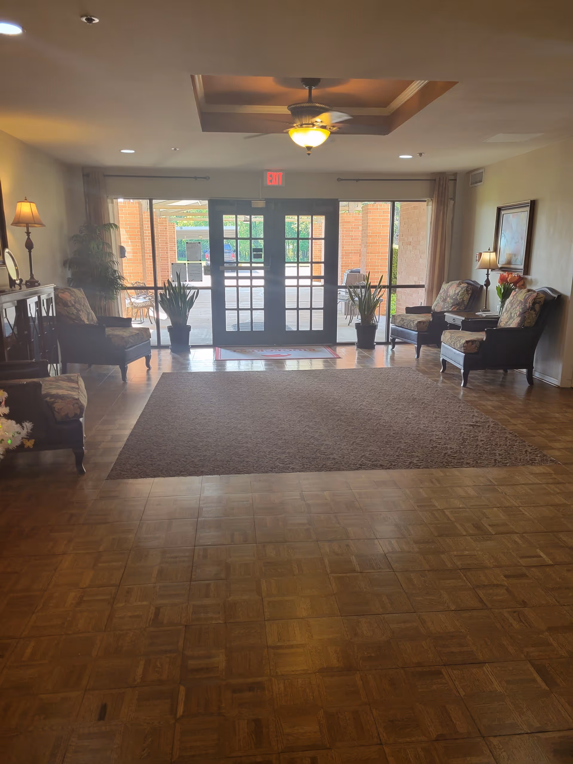 Entrance lobby with chairs, potted plants, and double glass doors leading outside.
