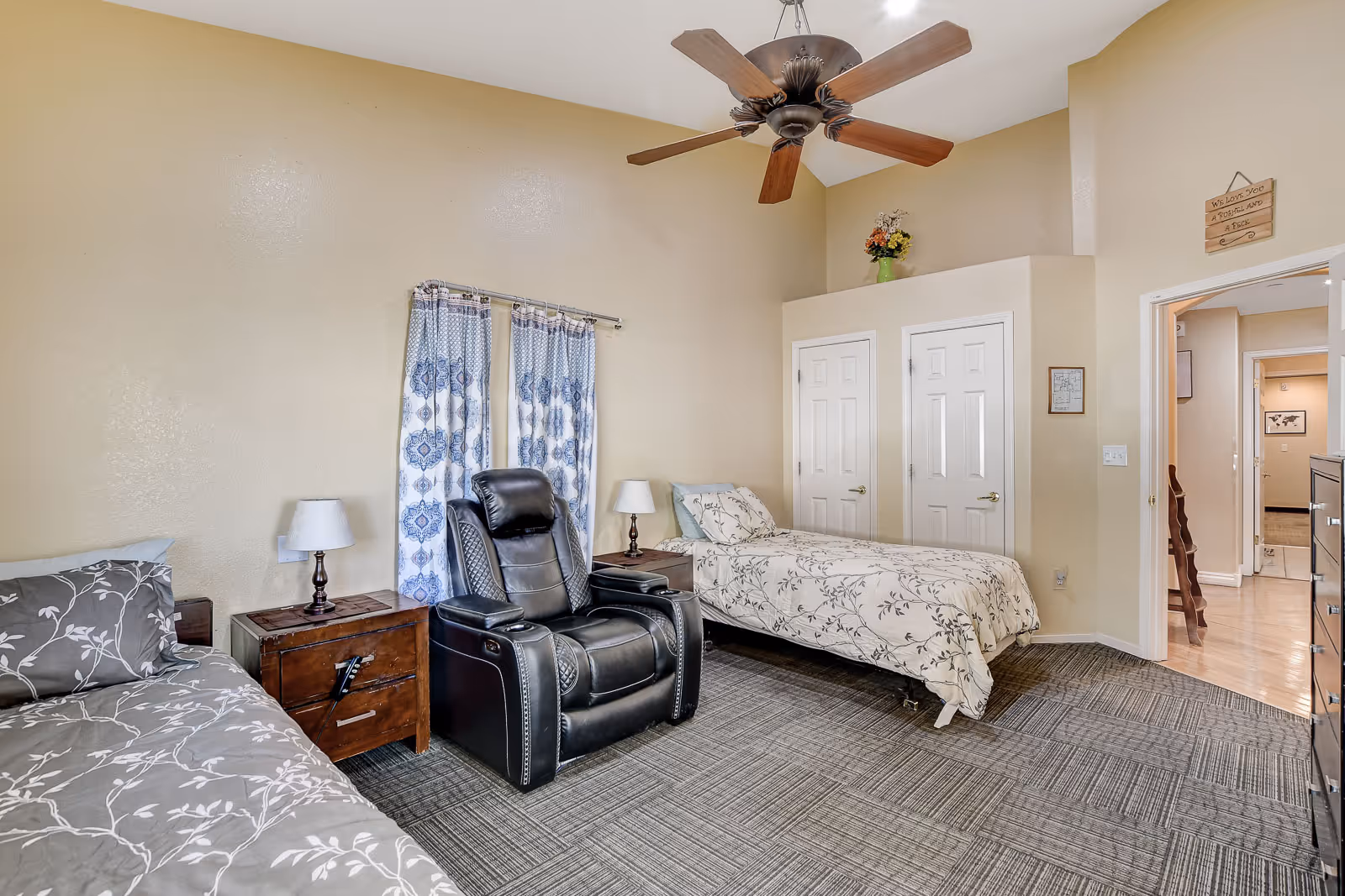A spacious bedroom with two beds, a black recliner, and a ceiling fan.