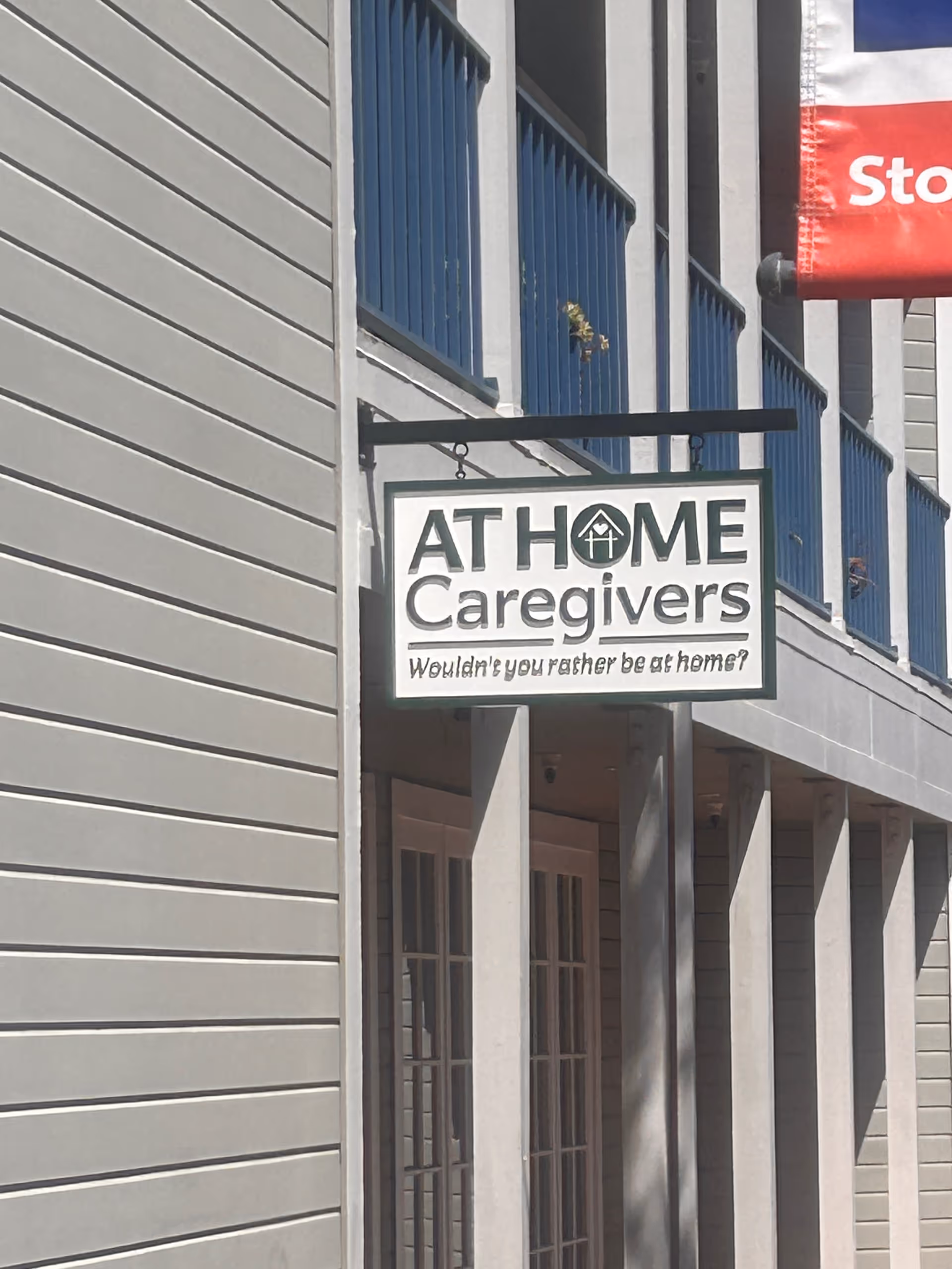 A sign for At Home Caregivers on the exterior of a gray building.