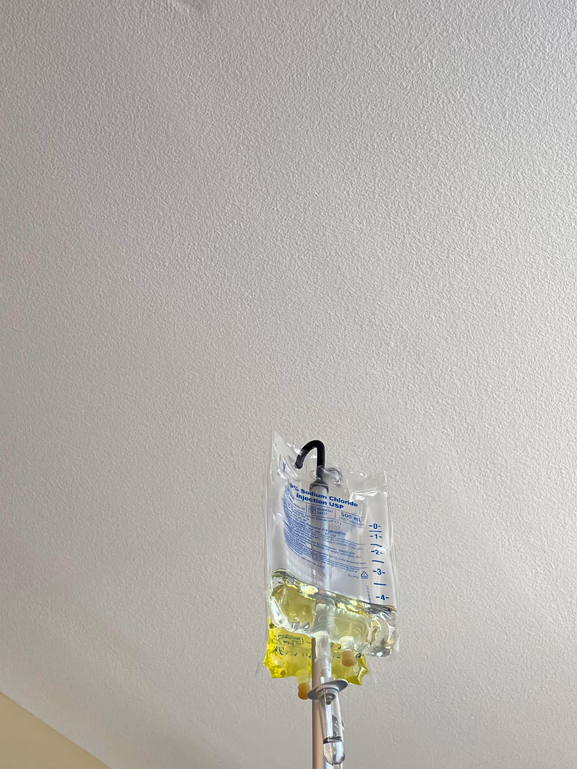 IV drip bag hanging from a pole against a textured white ceiling.