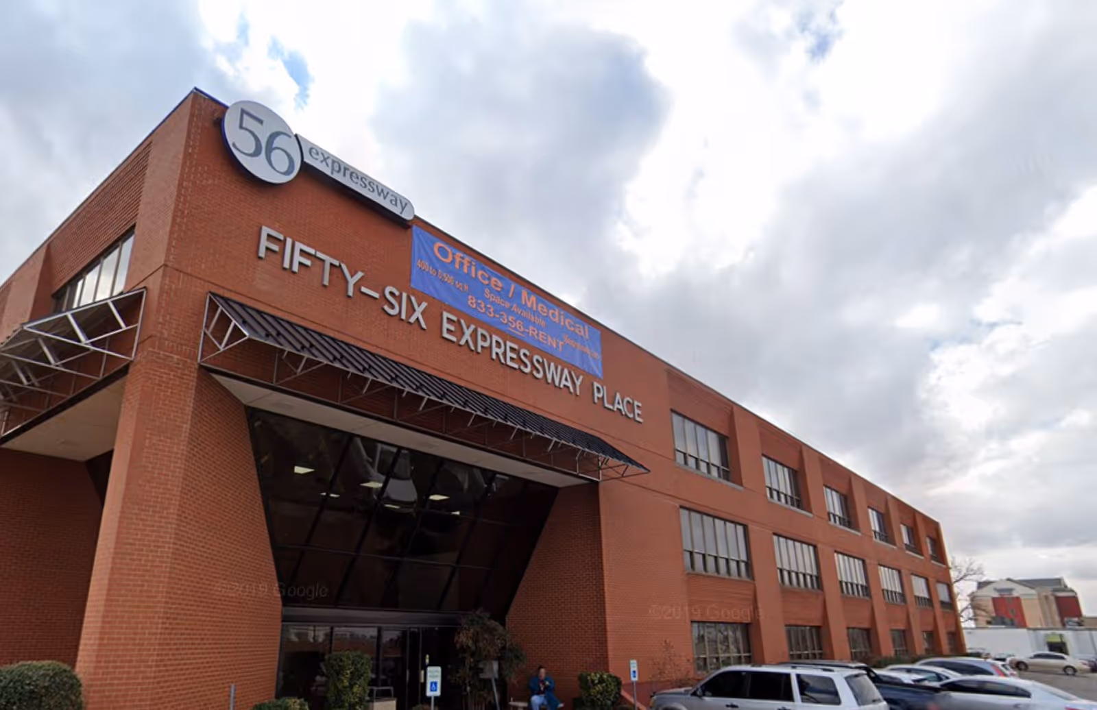 Red brick building front with Fifty-Six Expressway Place sign and parked cars.