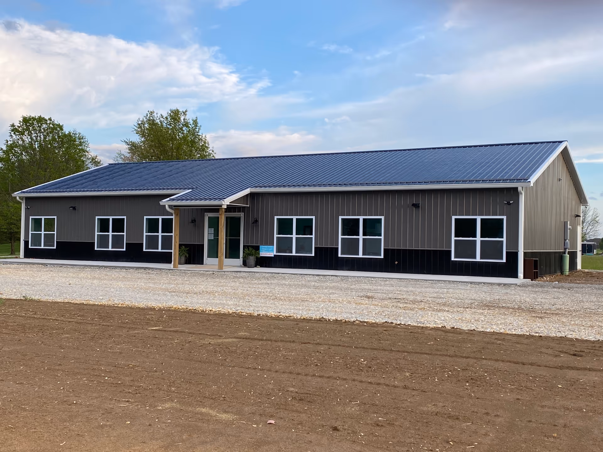 Single-story gray metal building with a blue roof, front entrance, and gravel lot.