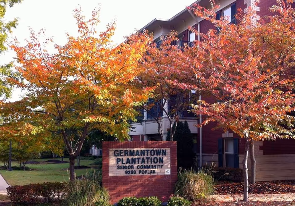 Exterior view of Germantown Plantation Senior Living Community with autumn trees and a brick sign.