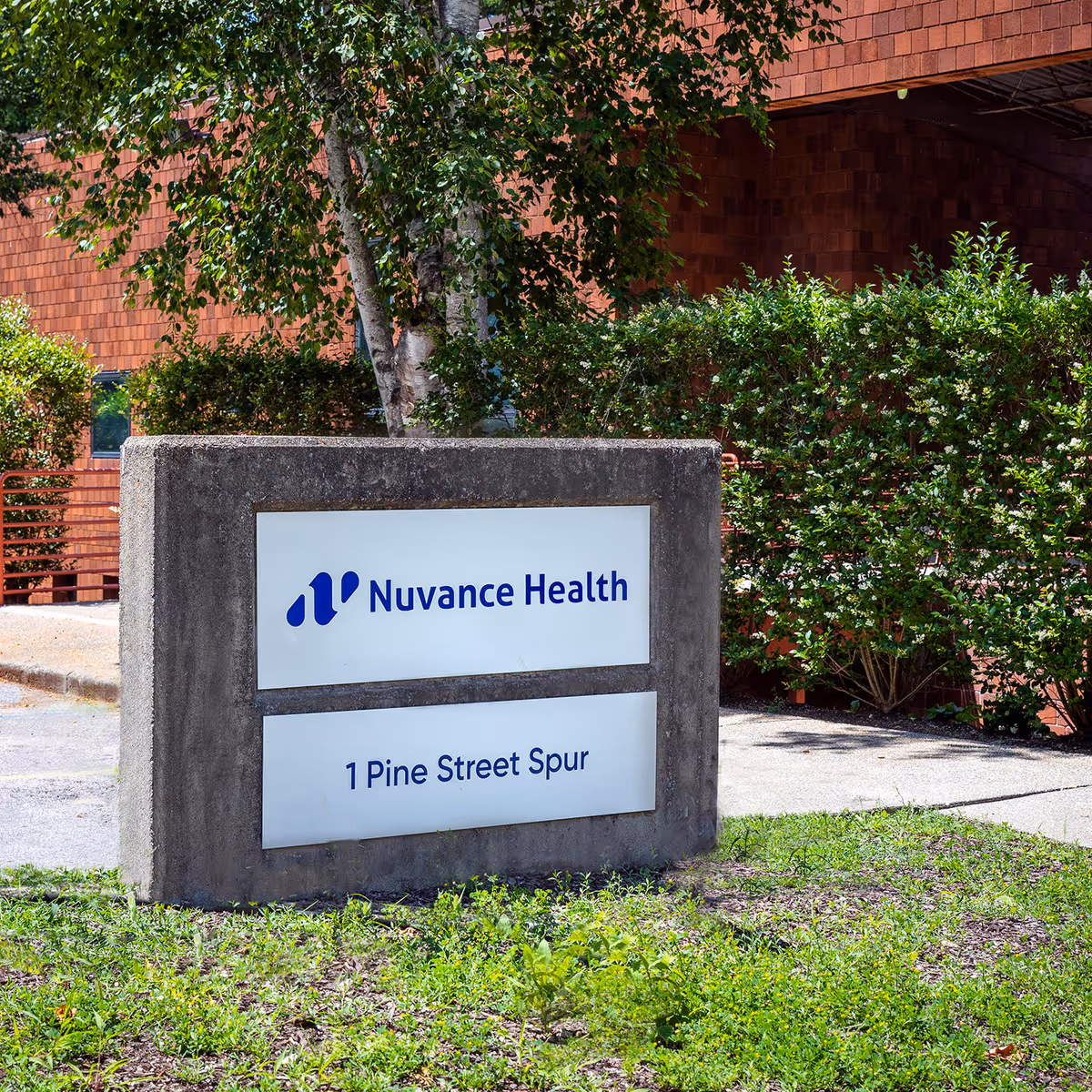 Concrete sign outdoors displaying Nuvance Health, with brick building and greenery in front.