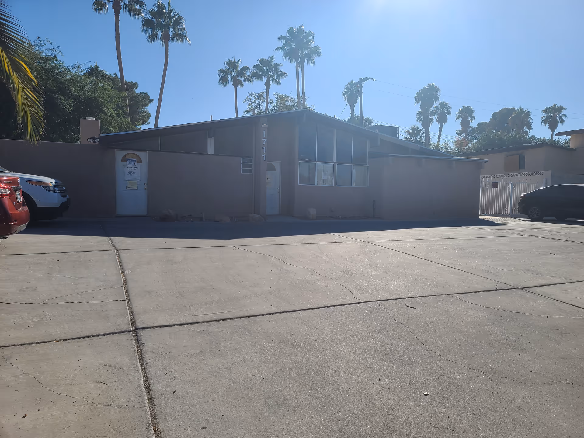 Front exterior of a small facility with parked cars and tall palm trees.