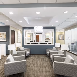 Reception lounge with gray seating, lamps, framed artwork, and a decorative central wall feature.