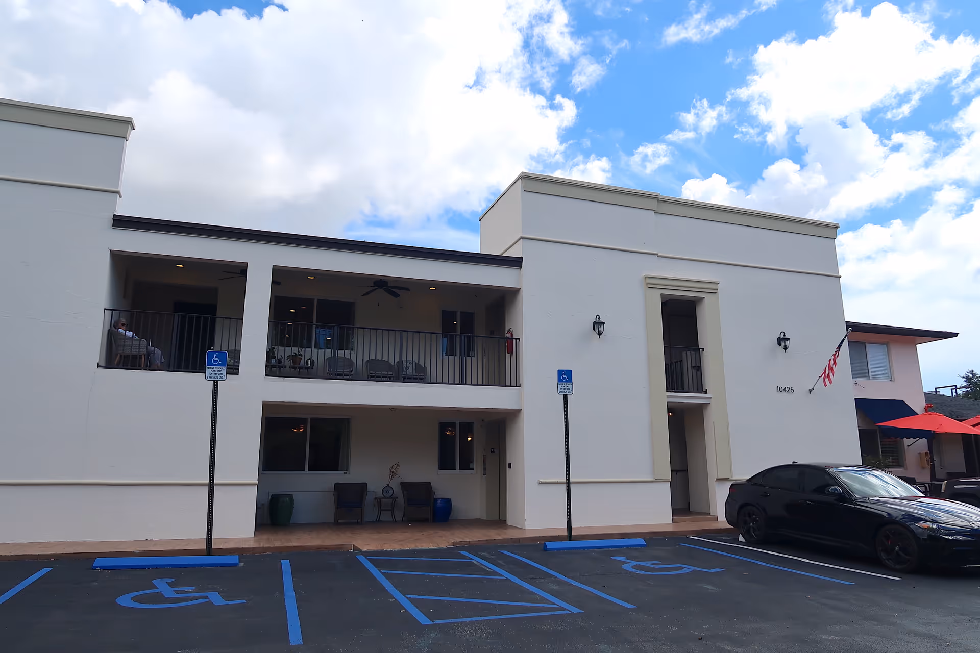 White modern senior housing building exterior with balconies, parking lot, and blue handicap spaces.