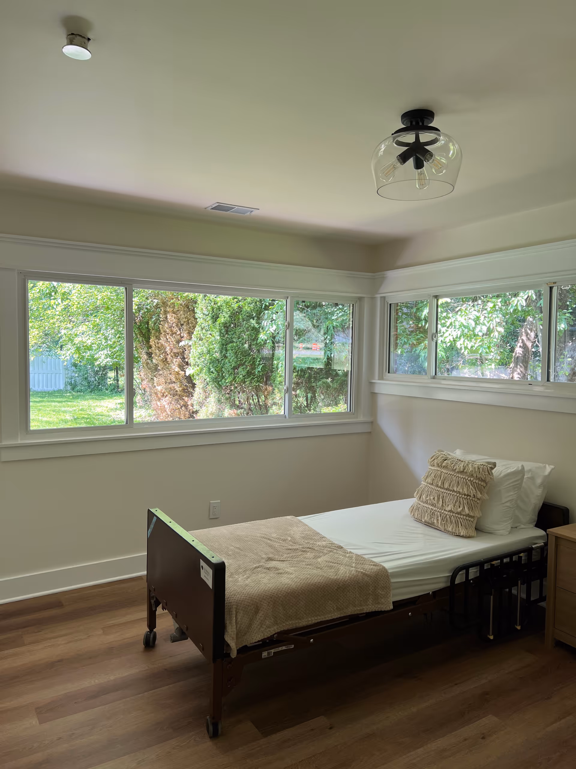 A single bedroom with a hospital-style bed, wooden floor, and large windows.